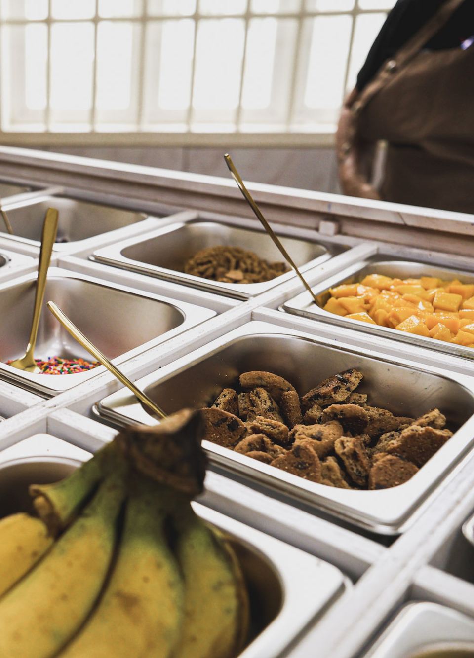 Cakuterie toppings bar with mango, cookies, sprinkles and bananas, served with gold spoons